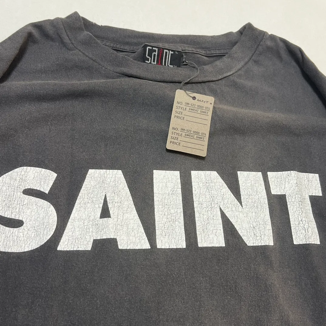 SAINT Mxxxxxx S>N>T LS TEE/BLACK Autumn and winter new style S>N>T slogan crack printed long TEE, washed black S-XL Asut ready-made garments dyed, the whole piece sprayed with horse-hair spray, and then sprayed again to fade the color. The collar and cuffs are frayed. Many hangings are worn NEW VINTAGE. Heavy craftsmanship.